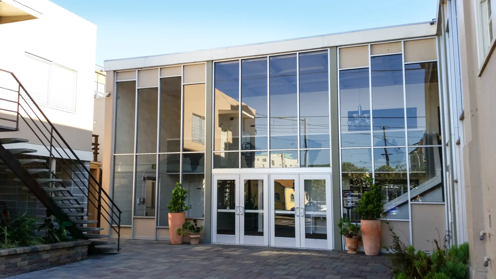 The school's glass courtyard entrance on a sunny day, with potted plants beside the doors