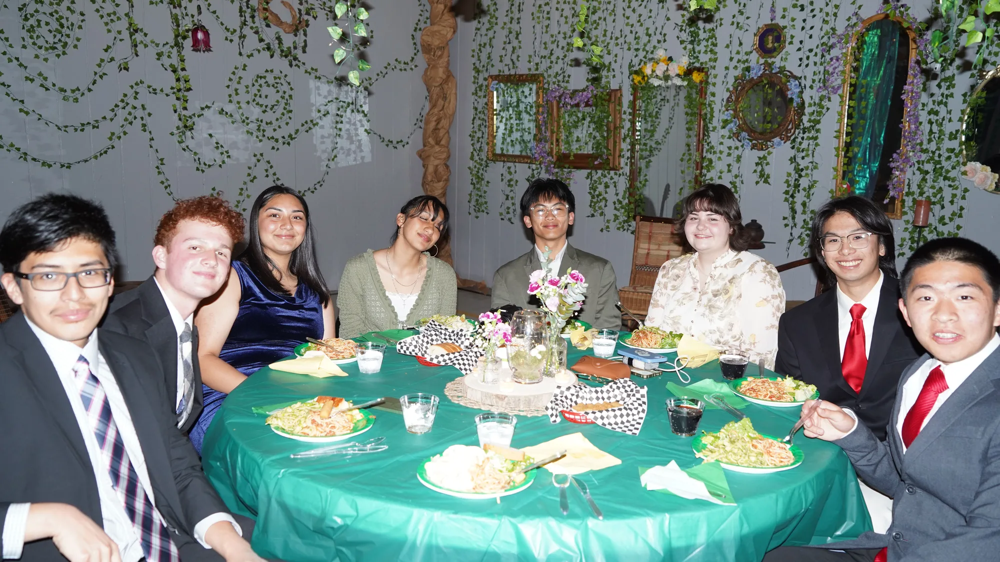 A table of high school students in formalwear smiling at the enchanted-forest banquet