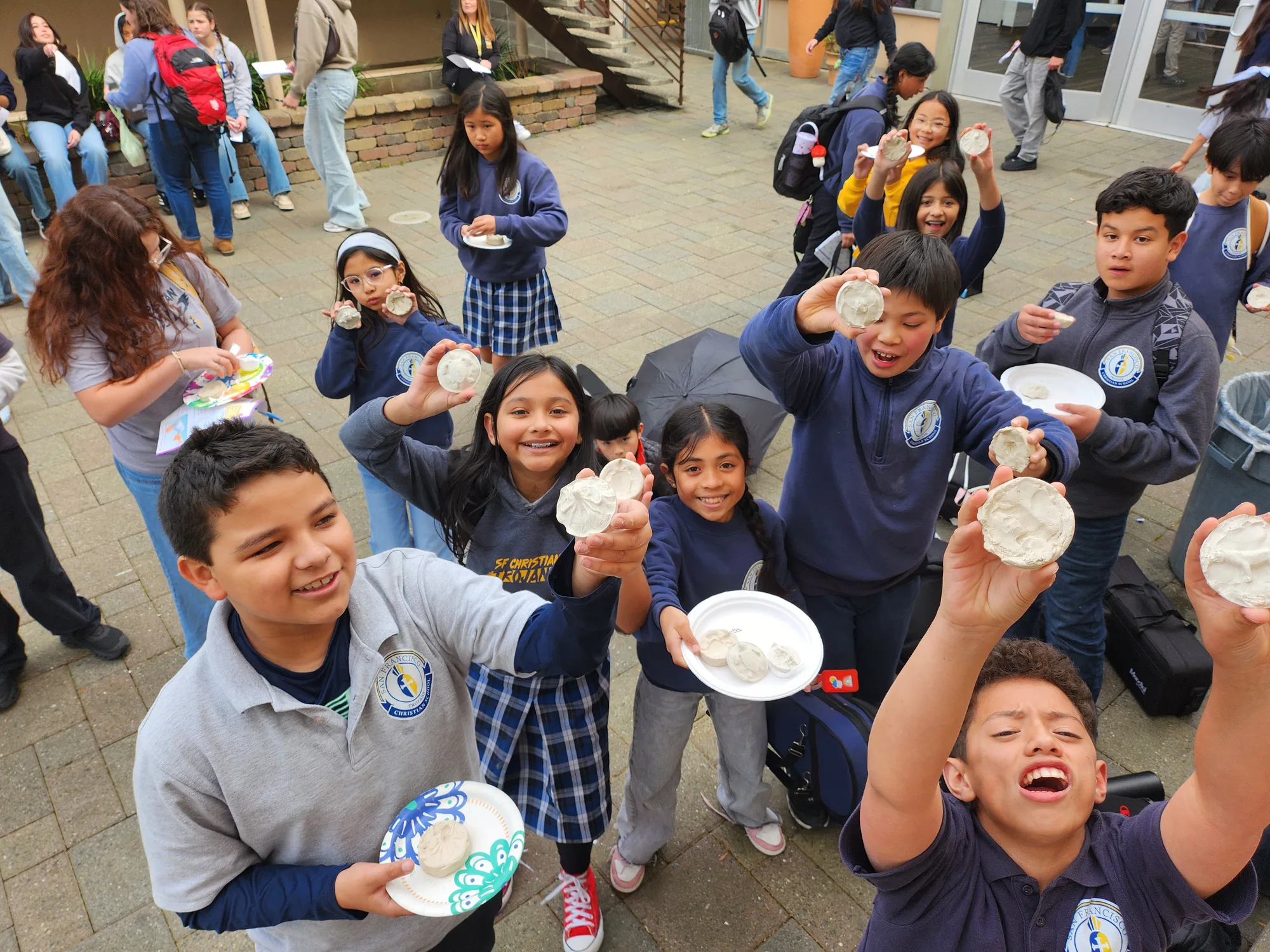 An overhead view of a class holding up their clay projects with big smiles