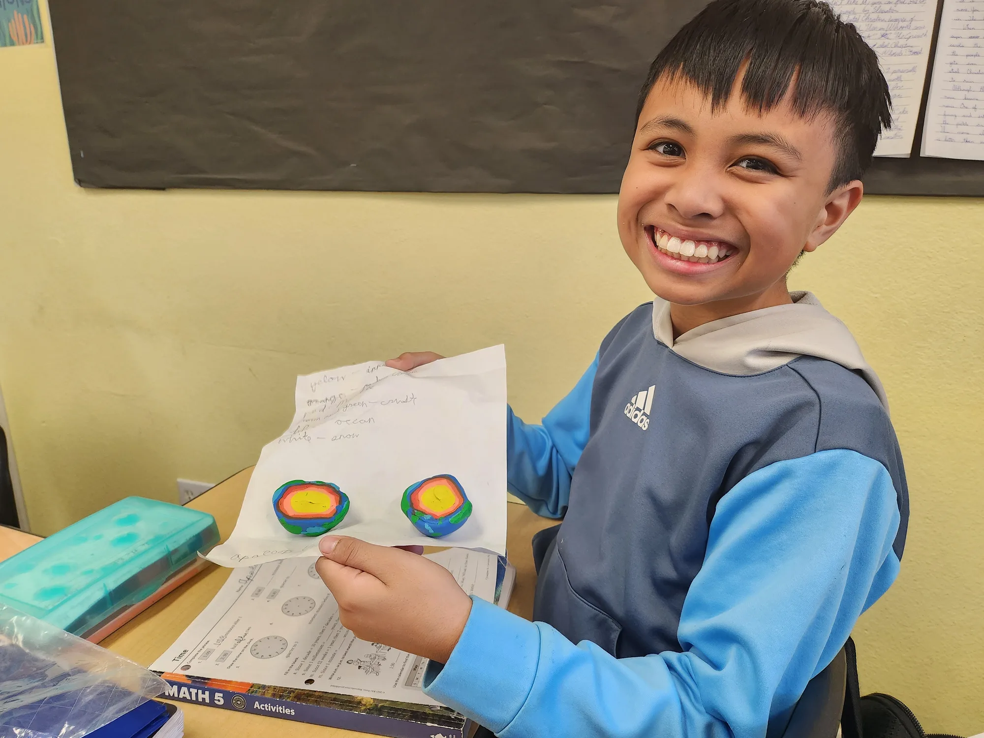A student smiling warmly while showing two clay models of the Earth's layers in class