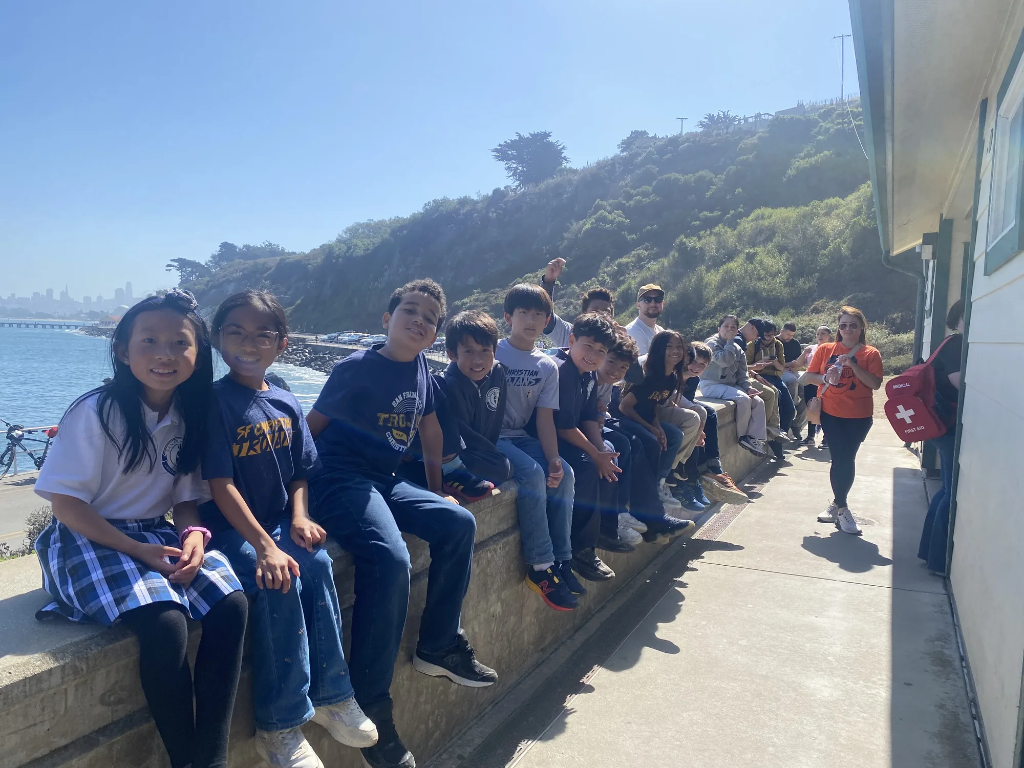A row of students on the seawall at Fort Point with the San Francisco skyline behind