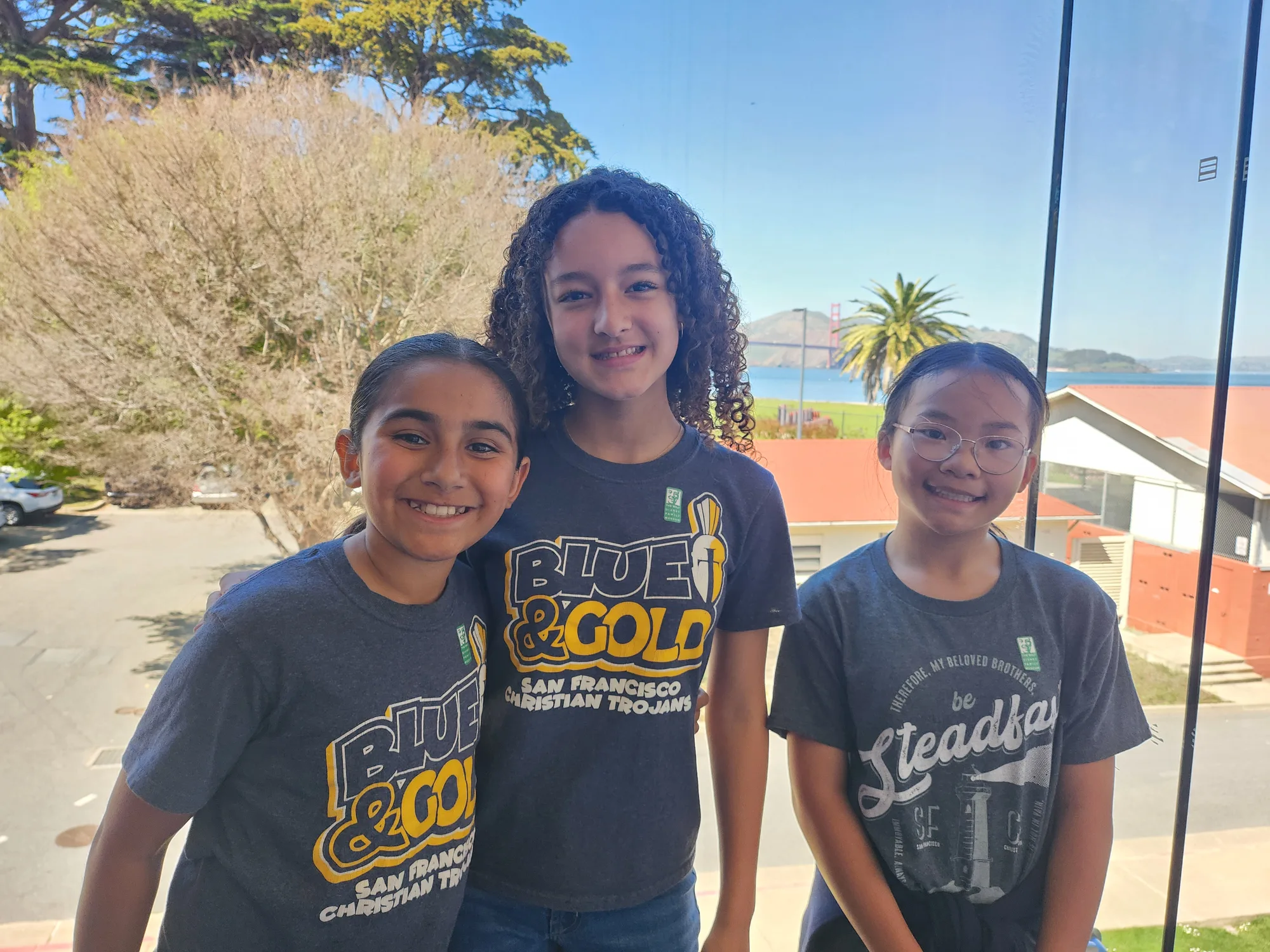 Three students smiling together before a window view of the Golden Gate Bridge