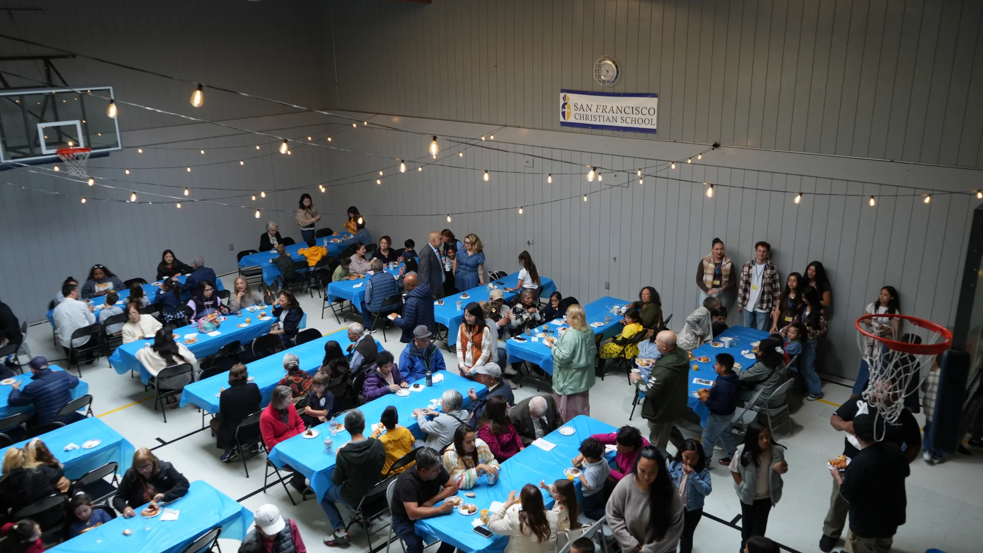The gym reception at Grandparents Day with blue tables, string lights, and the school banner