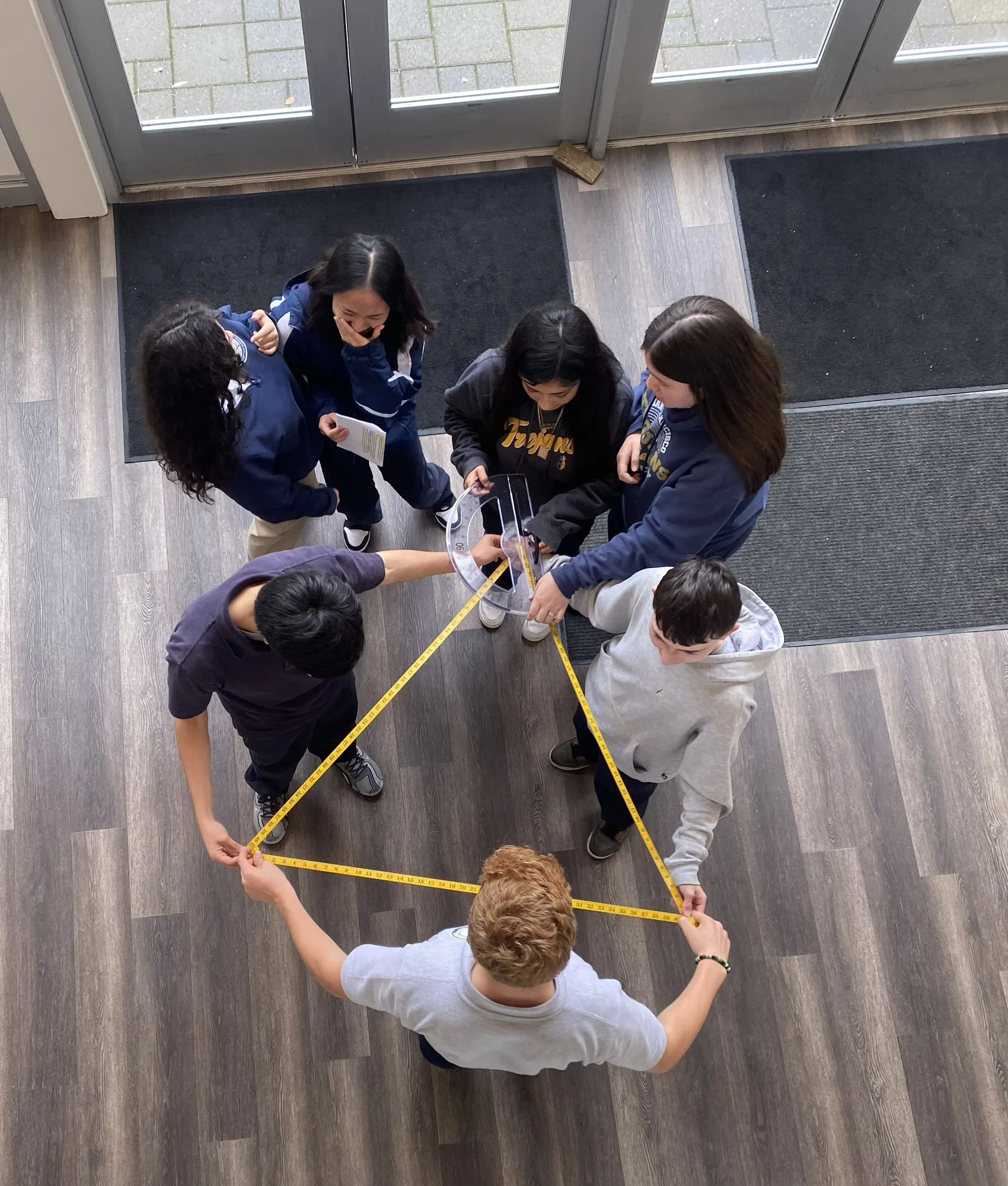 An overhead view of students forming a triangle with tape measures and a protractor