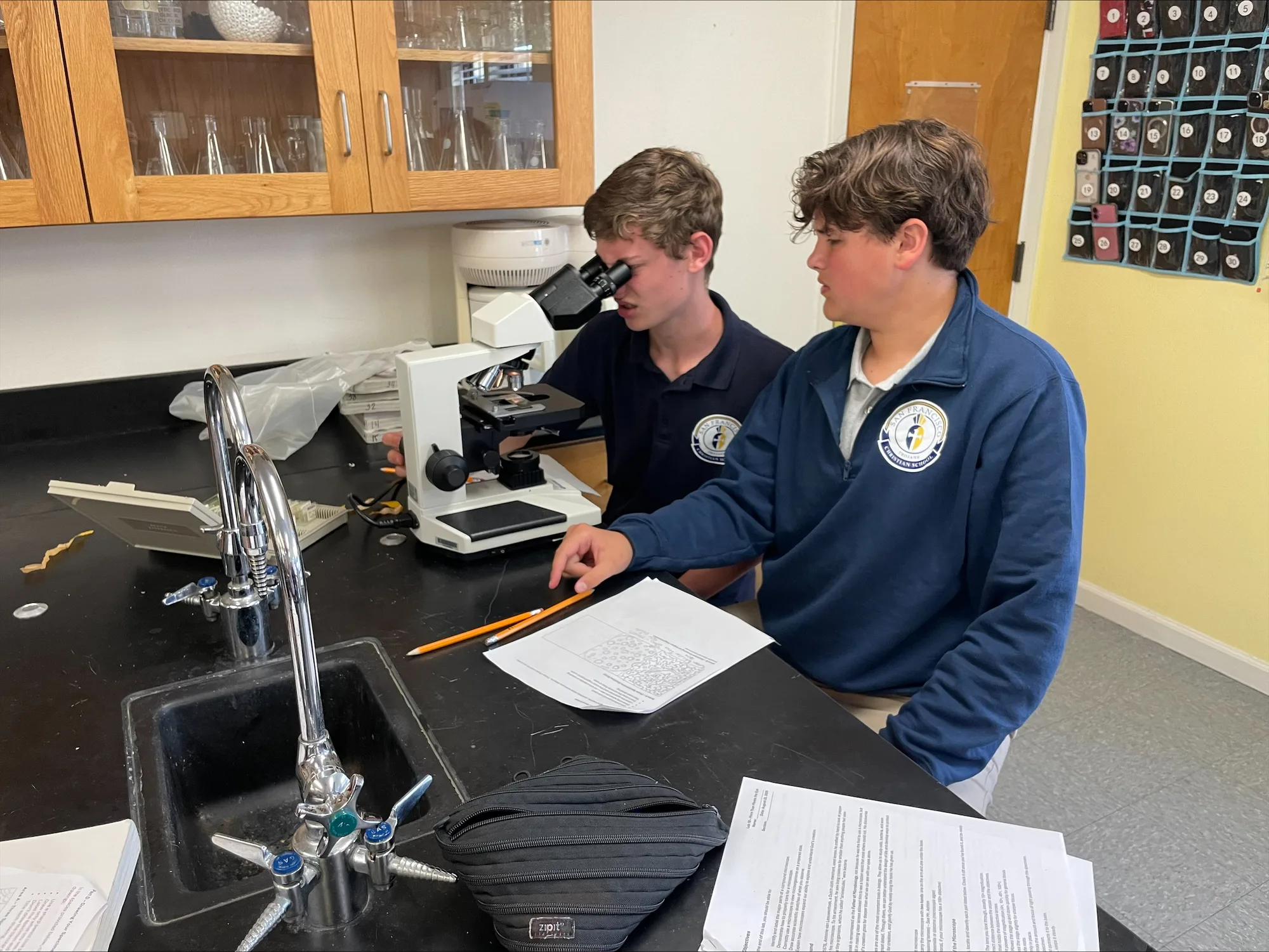 Two high school students working together at a microscope in warm light