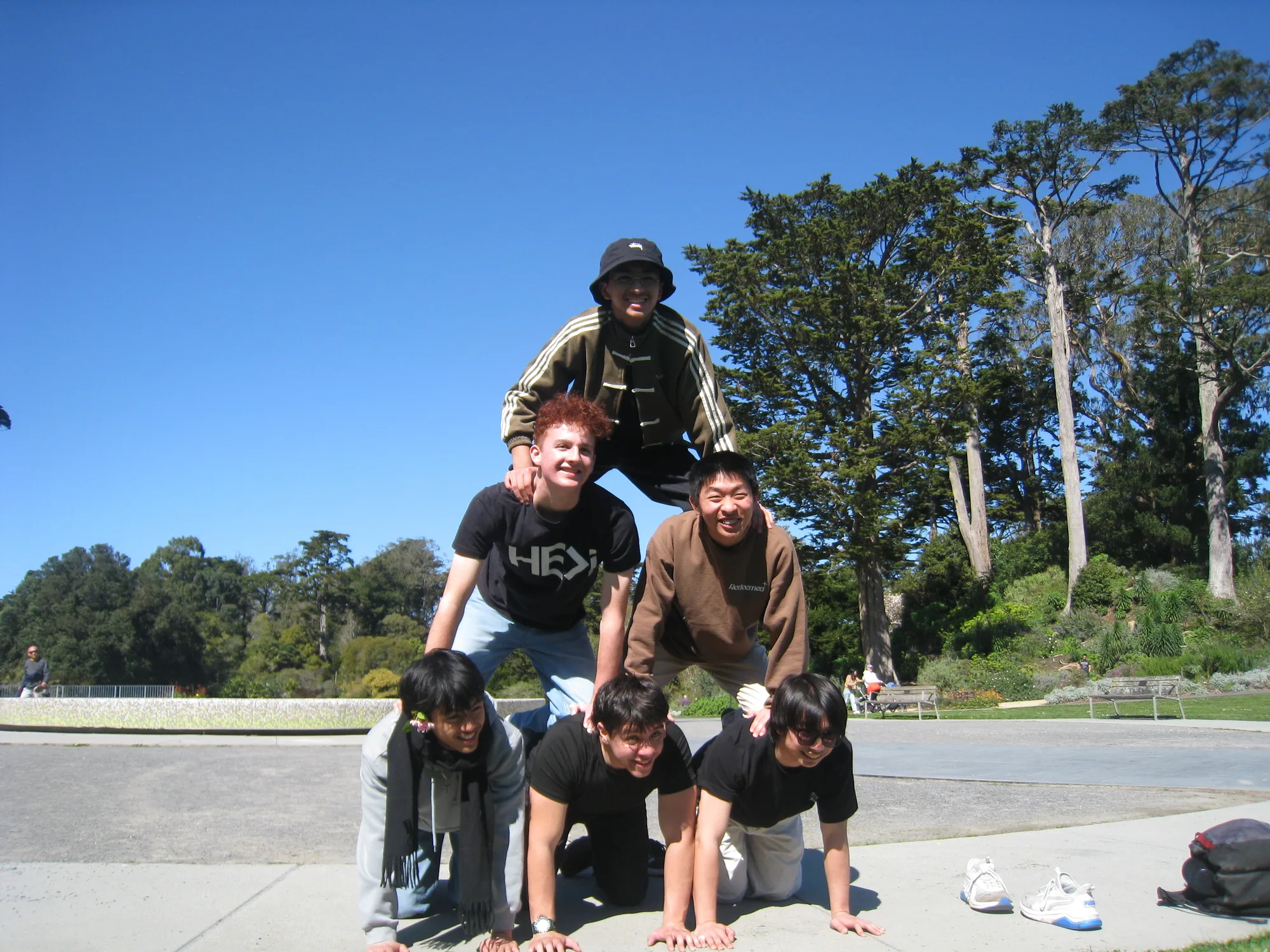 Six students forming a human pyramid under a blue sky, all smiling