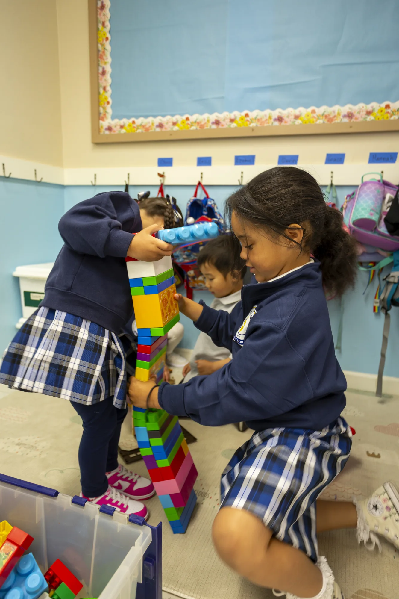 Two kindergarten girls building a tall colorful block tower together