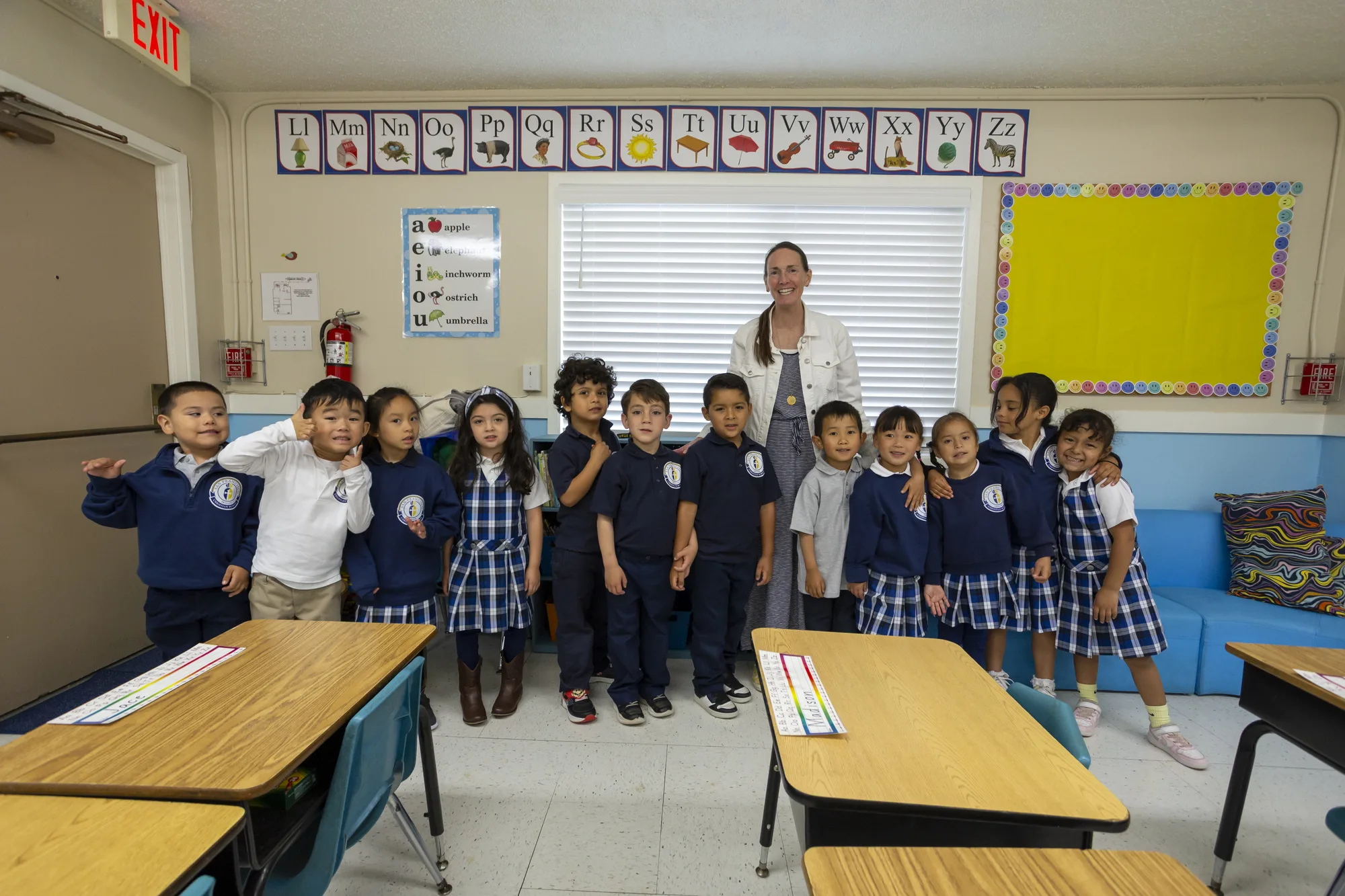 A kindergarten class posed with their teacher by the alphabet wall