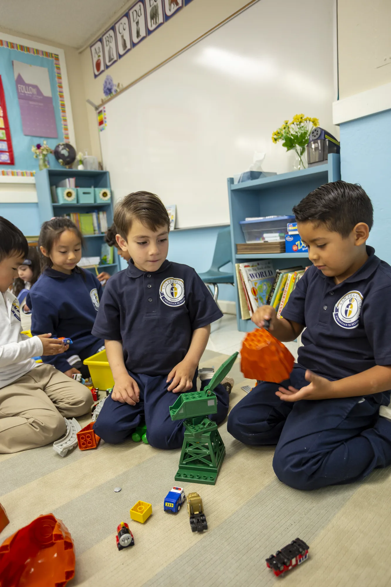 Three kindergarten boys playing with blocks and toy vehicles on the classroom floor