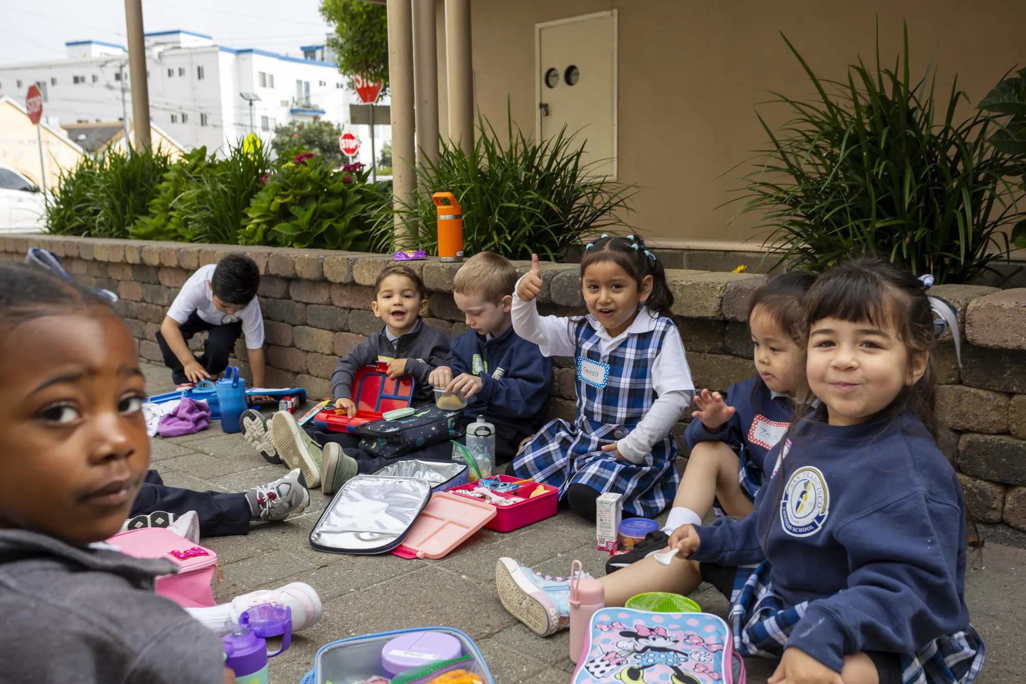 A student giving a thumbs-up among classmates eating lunch outdoors