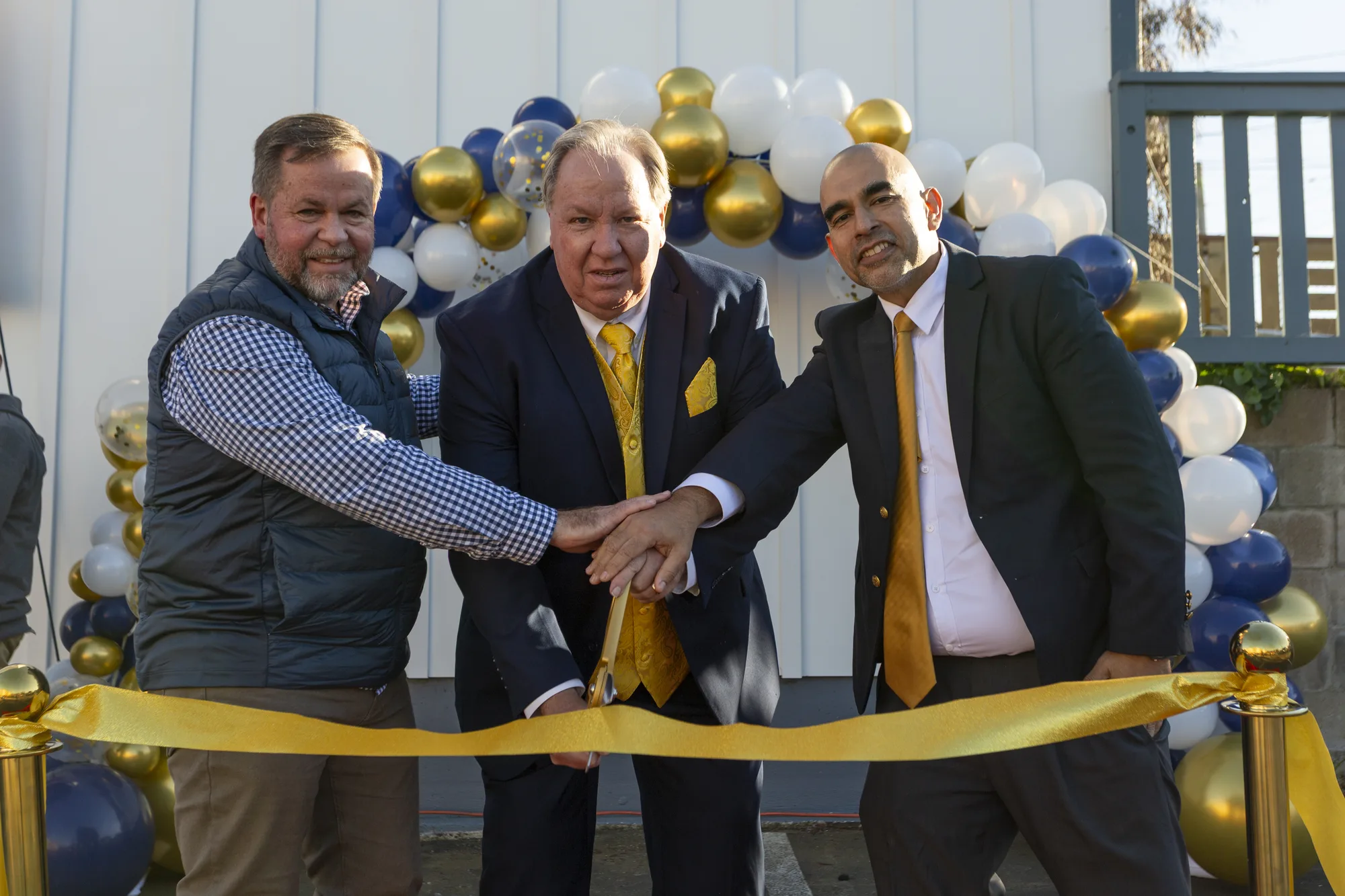 Three school leaders' hands together on giant gold scissors at the campus ribbon cutting