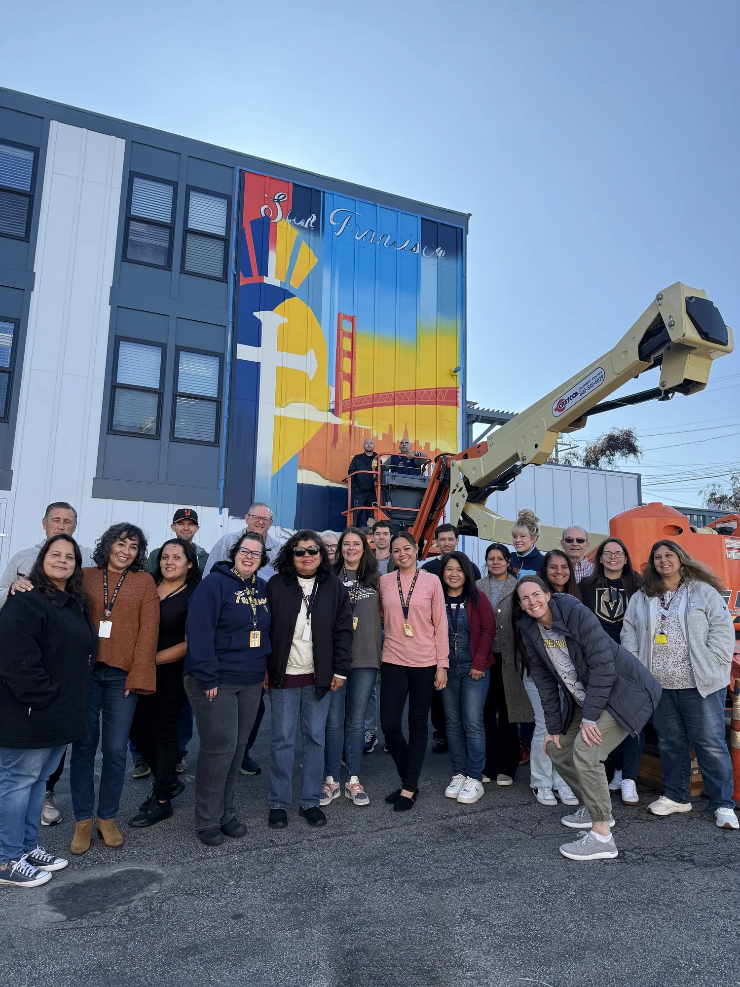 Staff gathered outdoors in front of a San Francisco mural on a sunny day