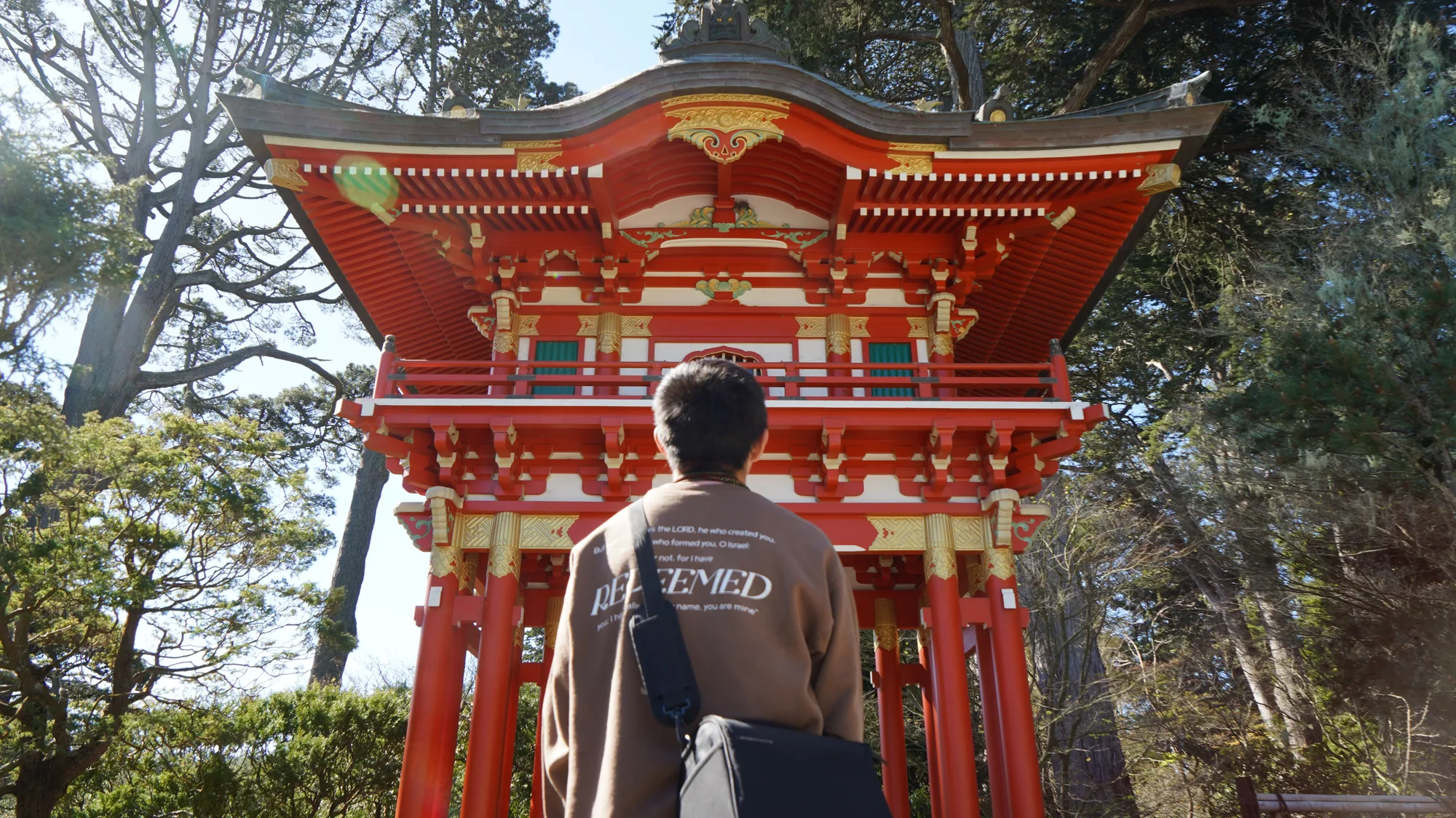 A student in a 'REDEEMED' sweatshirt looking up at the red pagoda in the Japanese Tea Garden