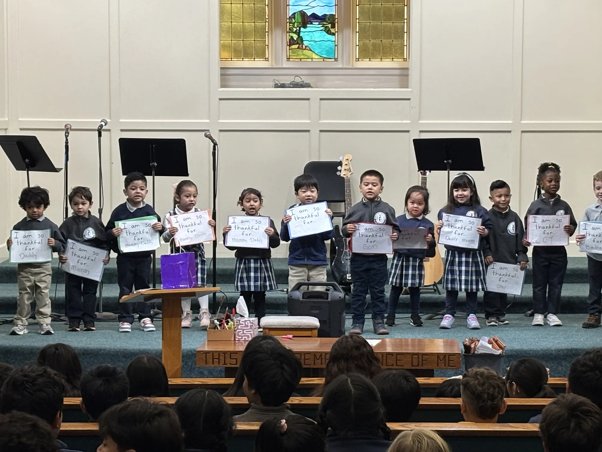 Kindergartners holding 'I am so thankful for God' signs at a Thanksgiving chapel