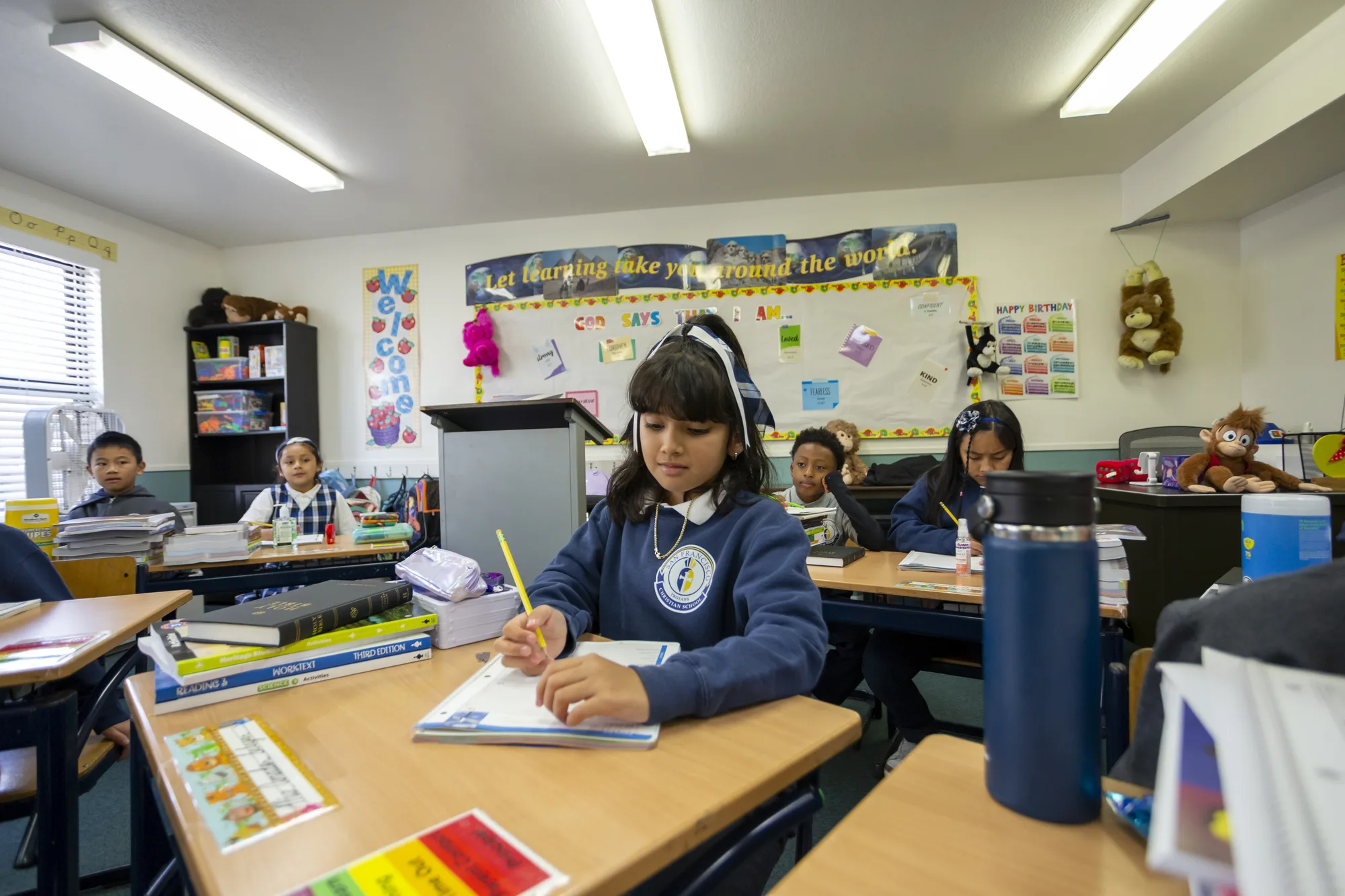A wide view of the third-grade classroom with a 'learning takes you around the world' banner