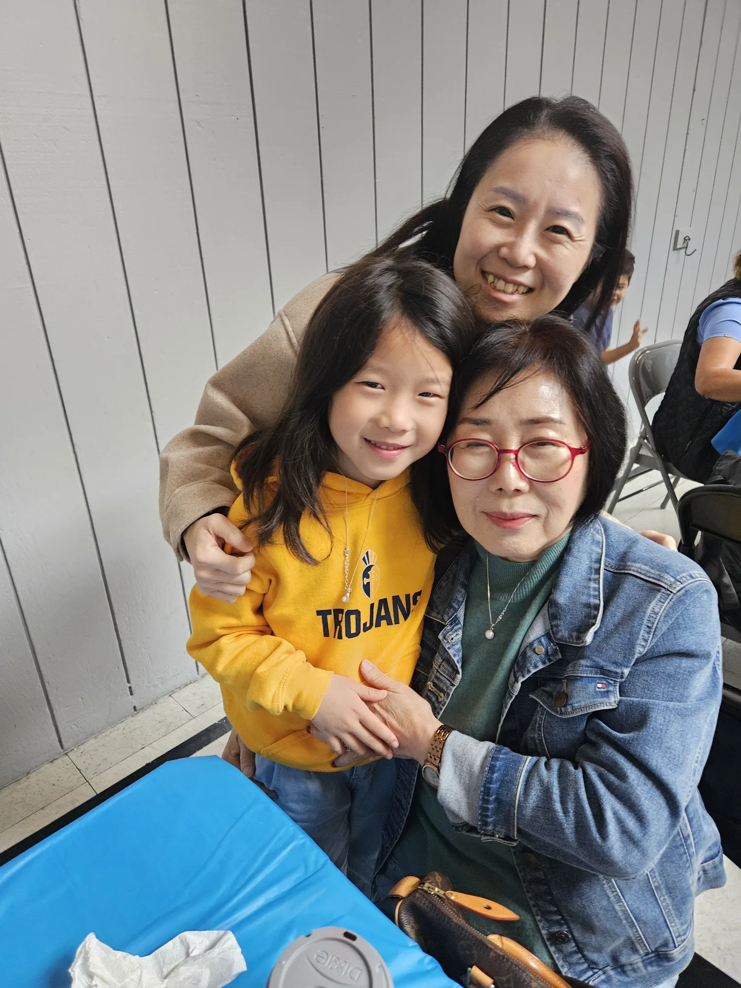 Three generations hugging at Grandparents Day, a mother, a student in a Trojans hoodie, and a grandmother