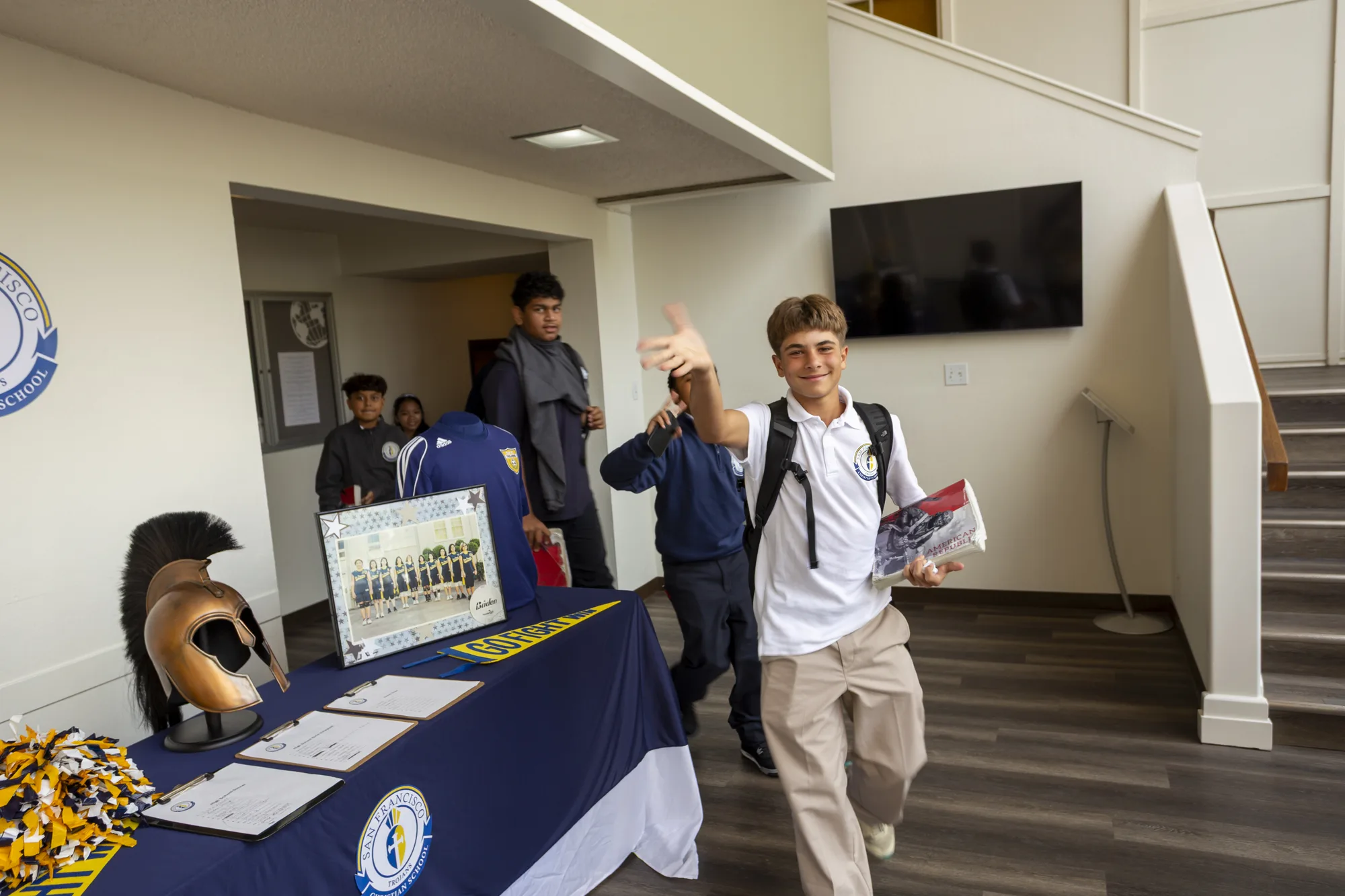A middle schooler grinning and pointing at the camera by the Trojans spirit display