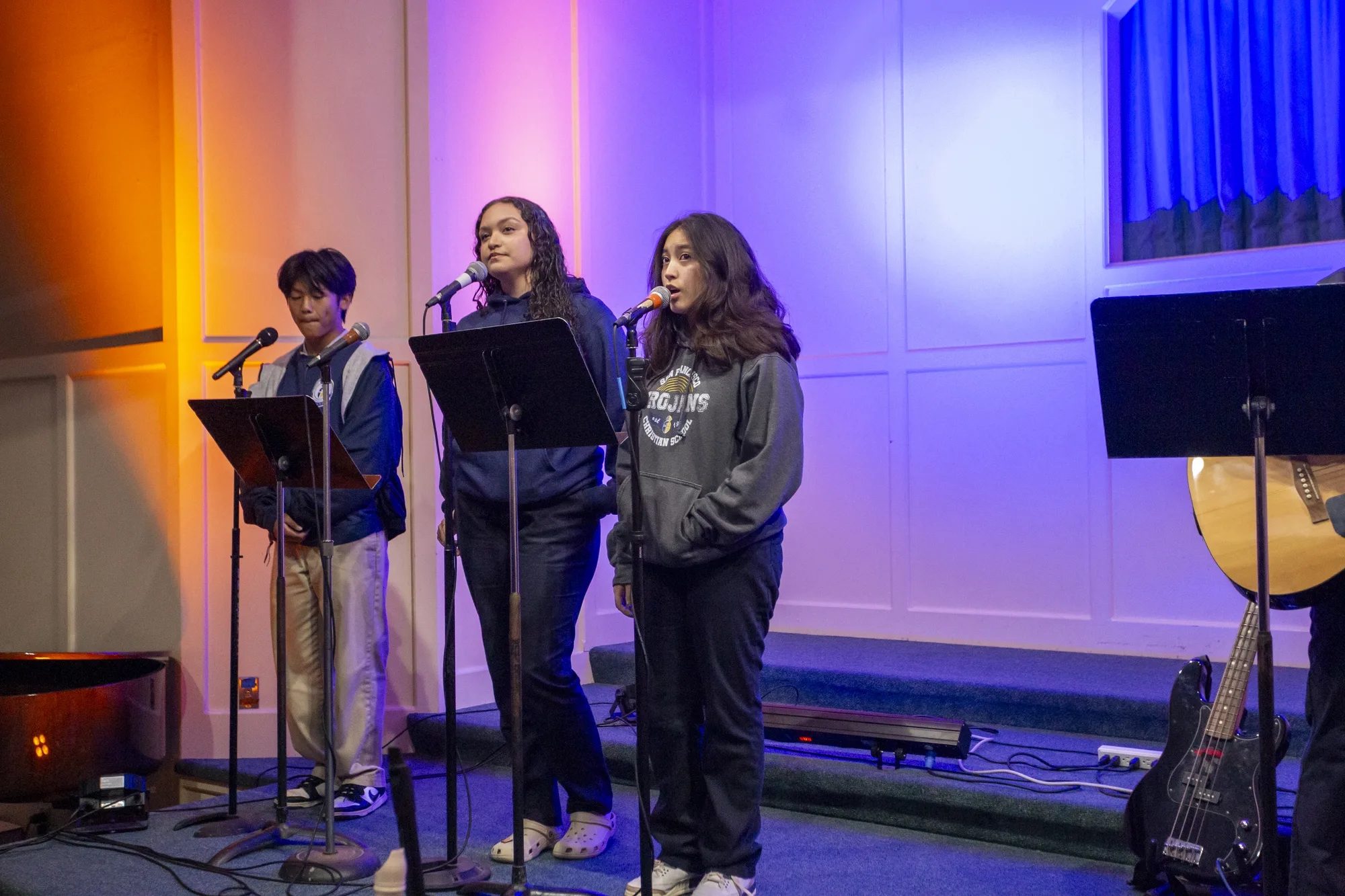 A student vocal trio leading worship in dramatic stage light